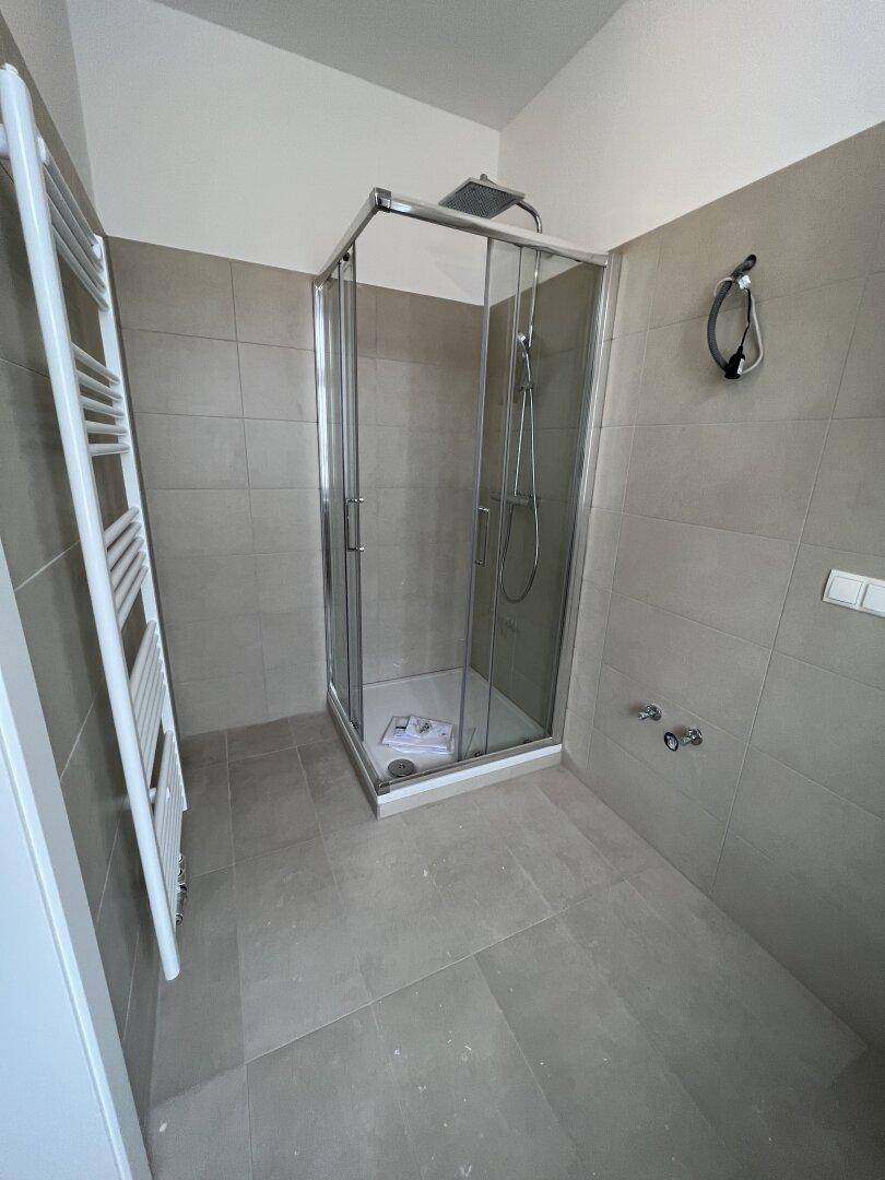 Modernes Badezimmer mit Duschkabine, grauen Fliesen und beheiztem Handtuchhalter.