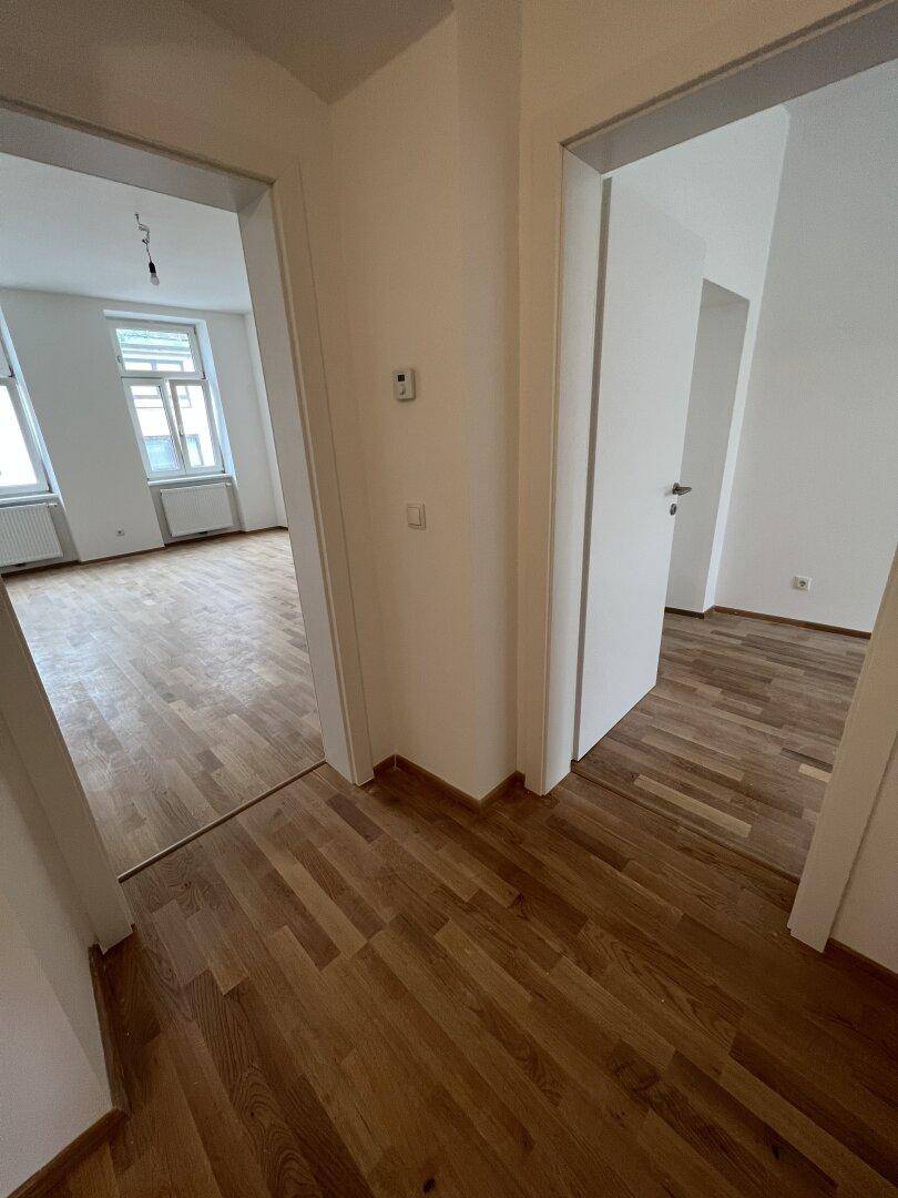Flur mit Holzboden und Durchgang zu einem weiteren hellen Zimmer, ideal für offene Gestaltung.