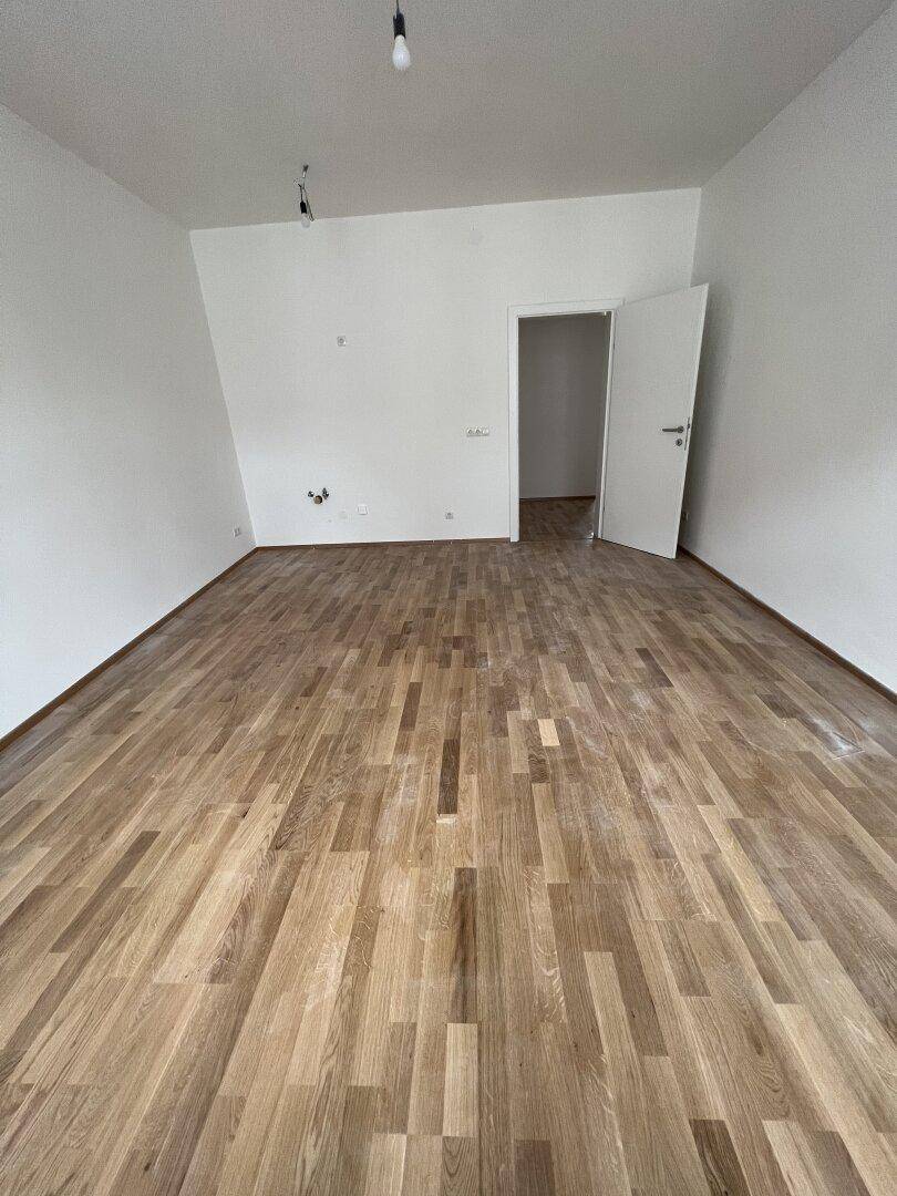 Geräumiger, heller Raum mit Holzboden und weiß gestrichenen Wänden, ideal für flexible Nutzung.