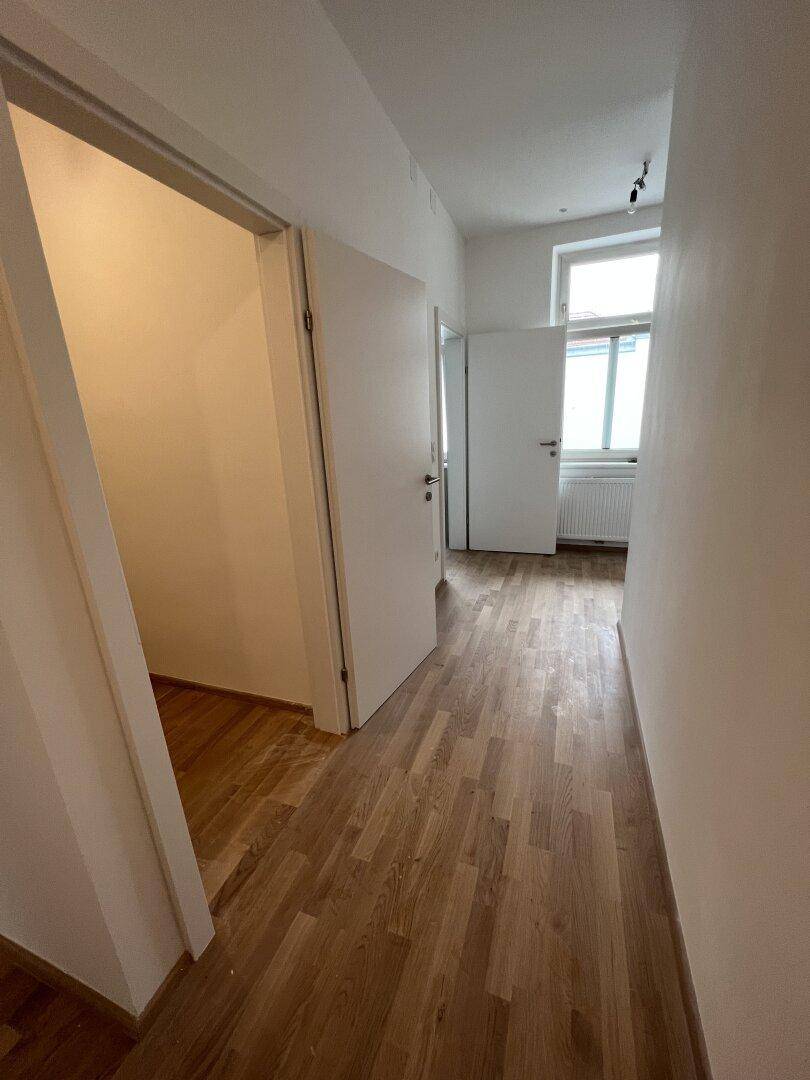 Heller Flur mit Holzboden und offenen Türen, die zu weiteren Zimmern mit Fenstern führen.