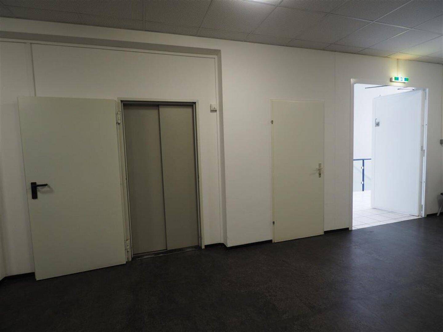 Heller Flur mit mehreren Türen und einem Aufzug, der Zugang zu den oberen Etagen bietet.