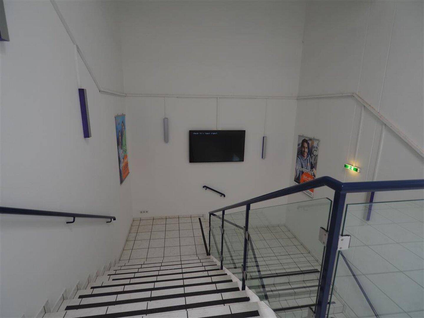 Blick von oben auf ein helles Treppenhaus mit Fliesenstufen und einem modernen Geländer.