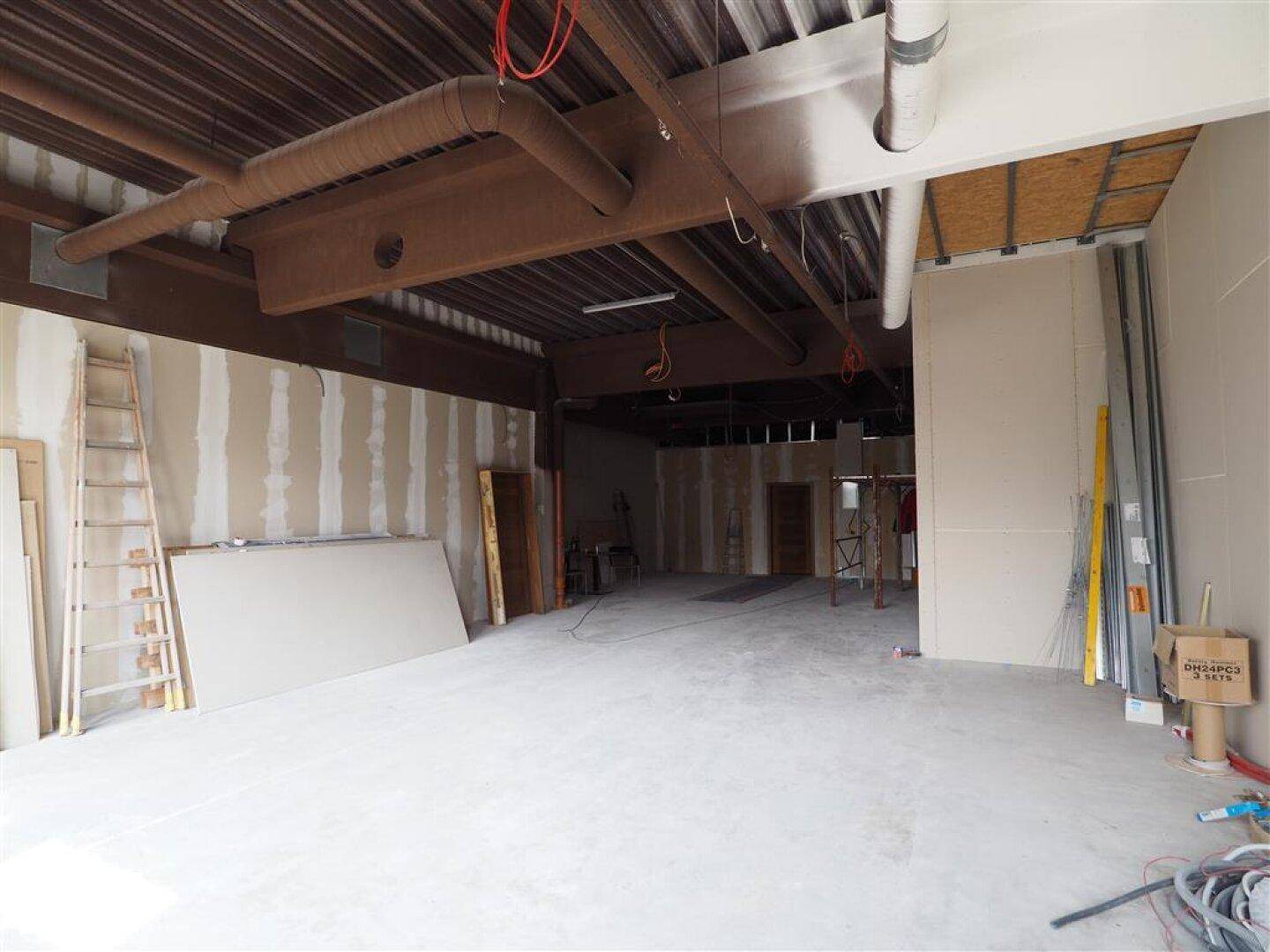 Weitläufiger Gewerberaum in Renovierung mit sichtbaren Deckenstrukturen und Baumaterialien.