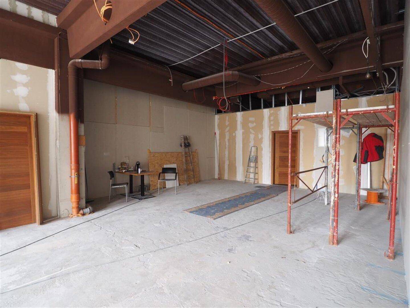Großer Gewerberaum im Rohbauzustand mit sichtbaren Installationen und Trockenbauwänden, bereit für den Ausbau.