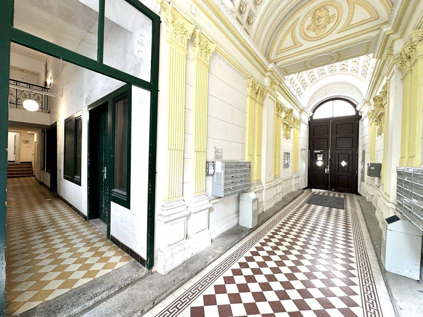 Historischer Eingangsbereich mit gemustertem Fliesenboden und verzierten Säulen.