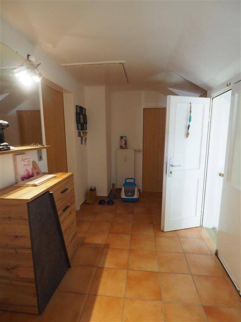 Heller Flur mit Terrakotta-Fliesenboden und Holzmöbeln, der zu weiteren Räumen führt.