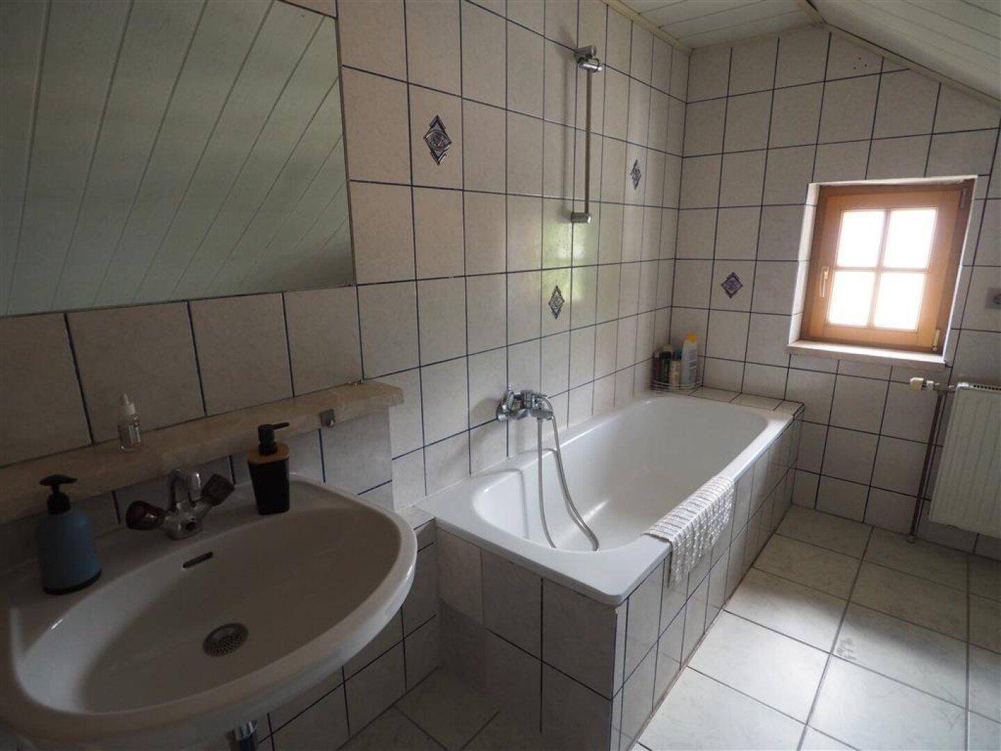 Gefliestes Badezimmer mit Badewanne, Waschbecken und Fenster für Tageslicht.