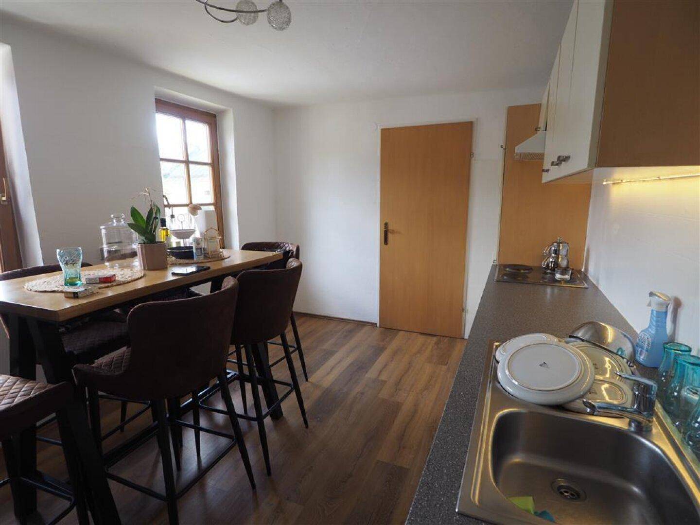 Funktionale Küche mit Essbereich, Holz-Laminatboden und Blick ins Grüne durch das Fenster.