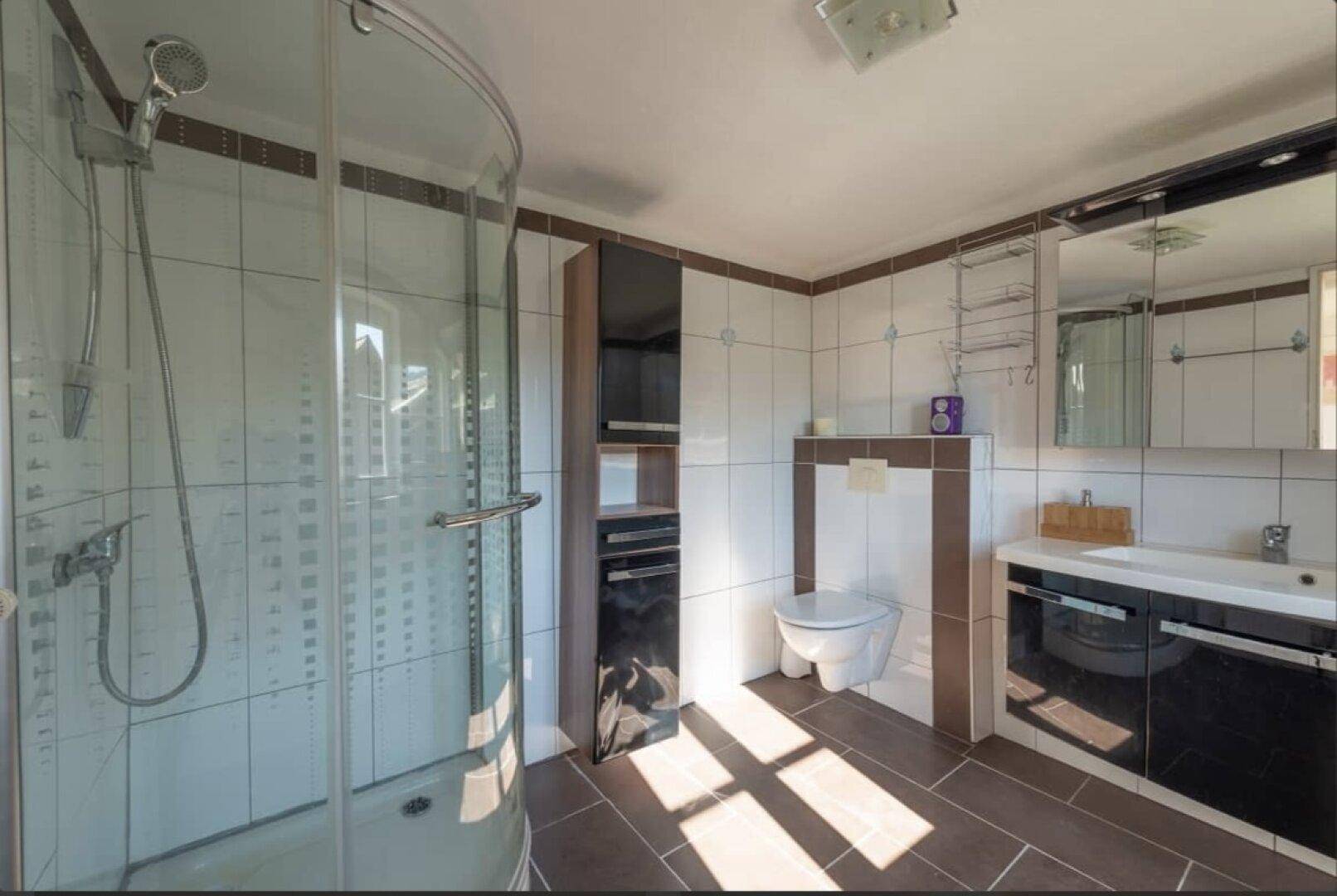 Modernes Badezimmer mit Duschkabine, Wand-WC und dunklen Bodenfliesen.