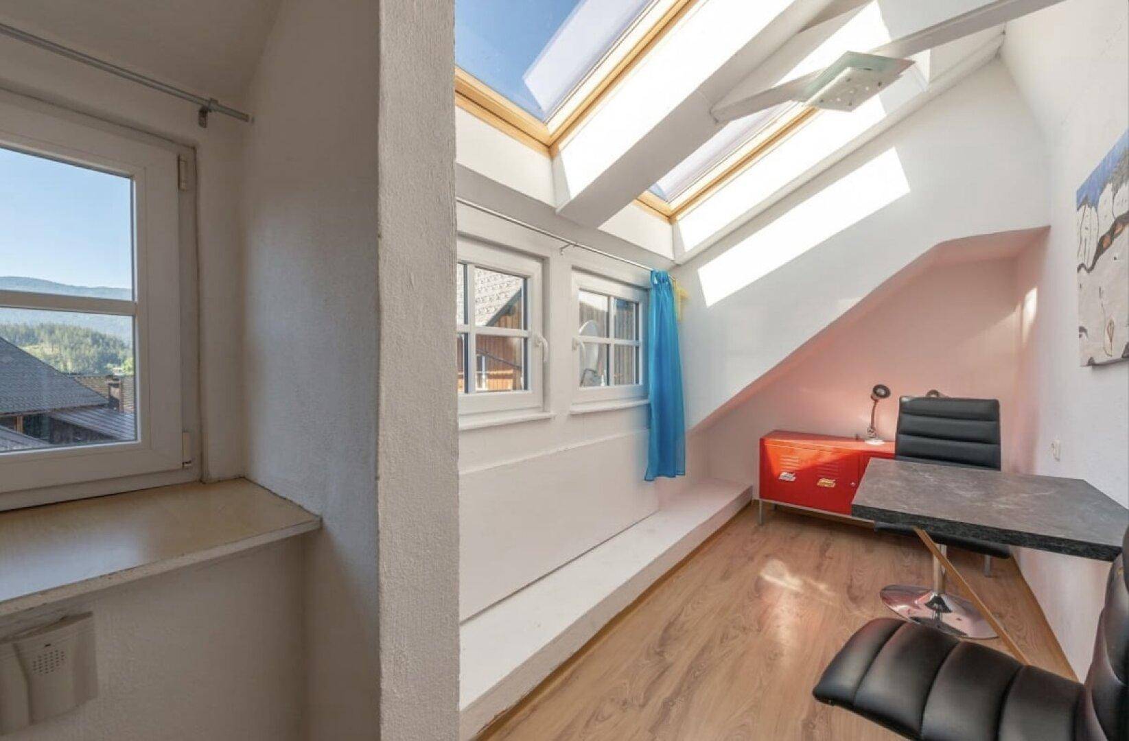 Heller Arbeitsbereich unter dem Dach mit Schreibtisch, Stuhl und großen Dachfenstern.