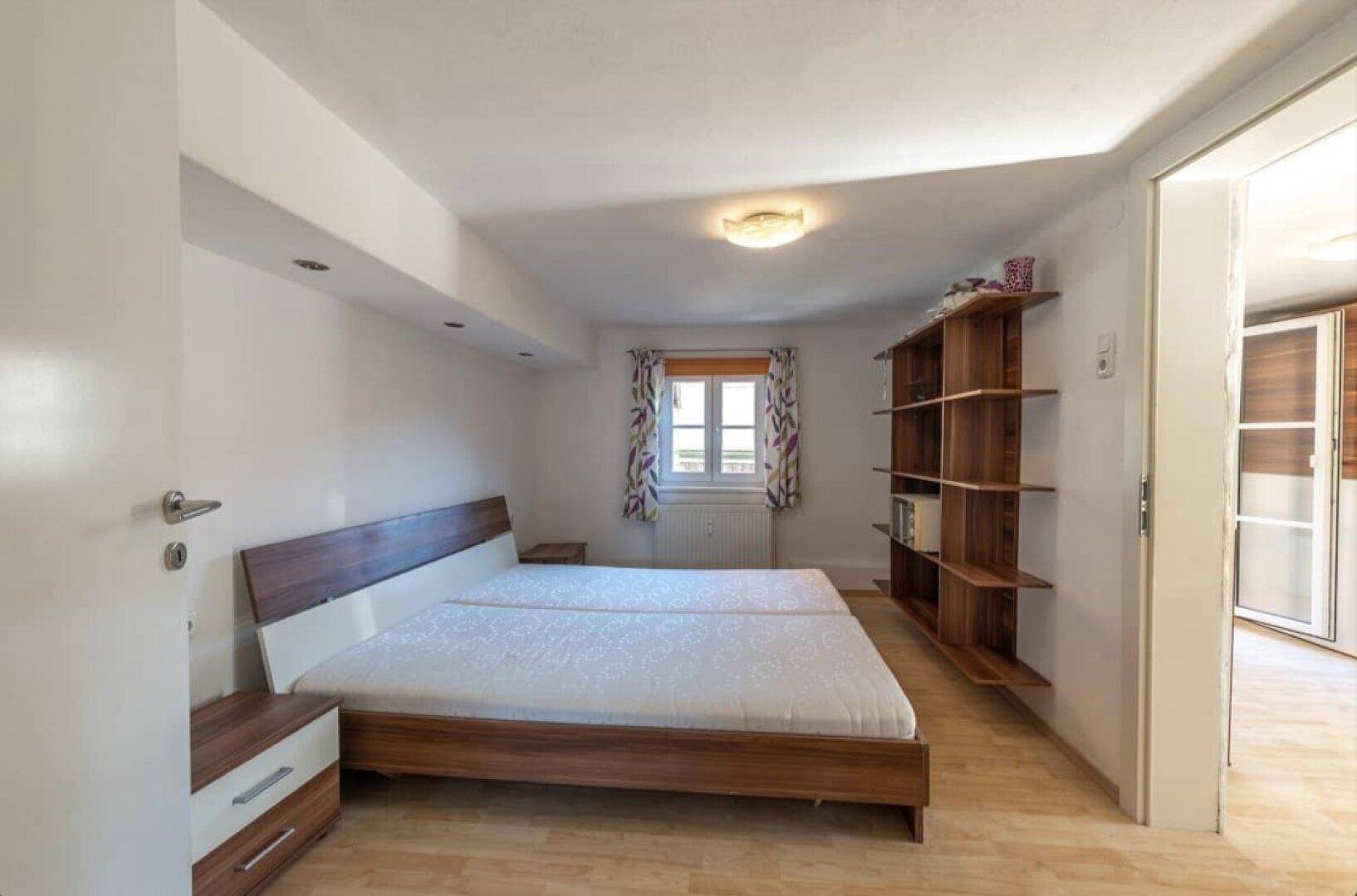 Geräumiges Schlafzimmer mit Doppelbett, Holzboden und praktischen Regalen.