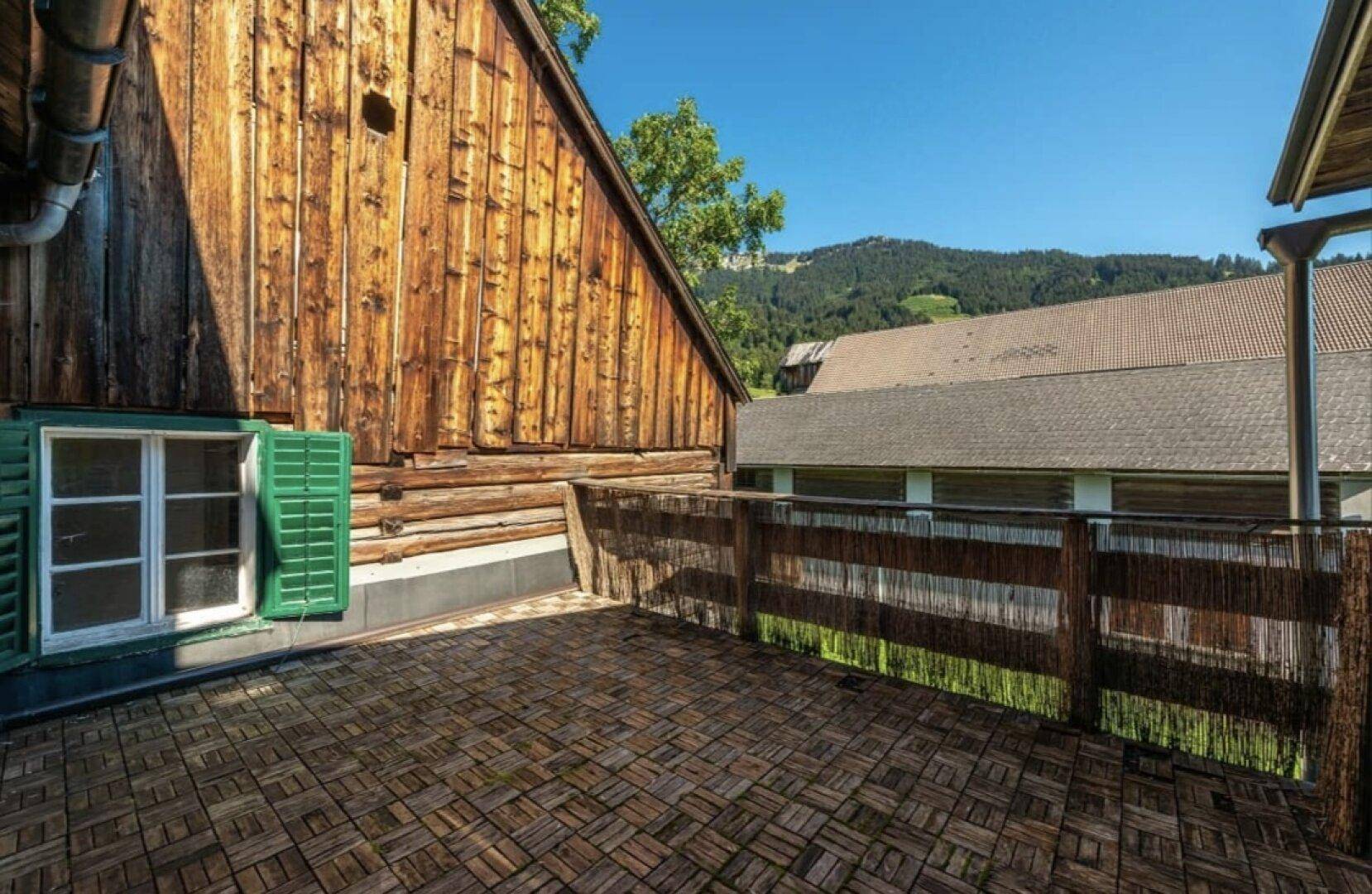 Sonniger Außenbereich mit Holzbodenfliesen und Blick auf die bewaldeten Hügel.