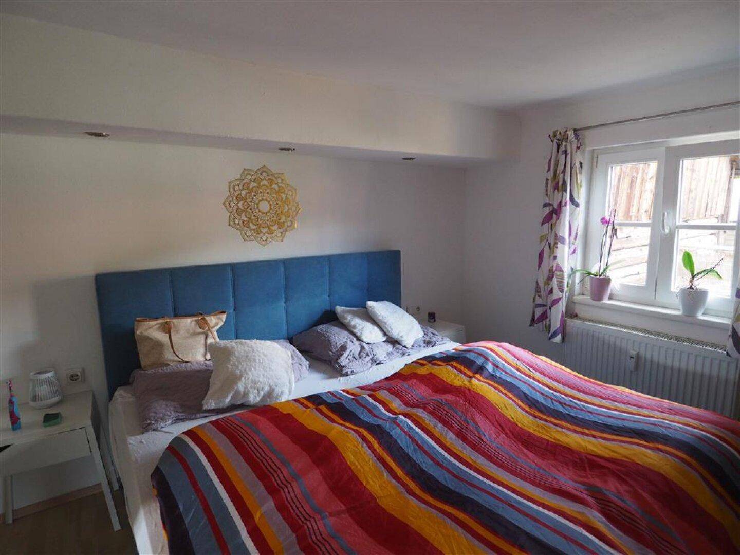 Helles Schlafzimmer mit Doppelbett, farbenfroher Bettwäsche und Fensterblick.