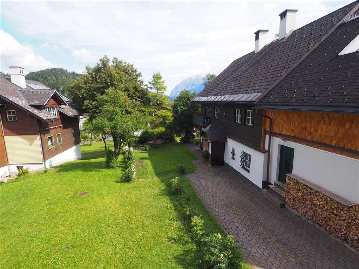 Großer grüner Gartenbereich mit gepflasterter Auffahrt und Blick auf die umliegenden Berge.