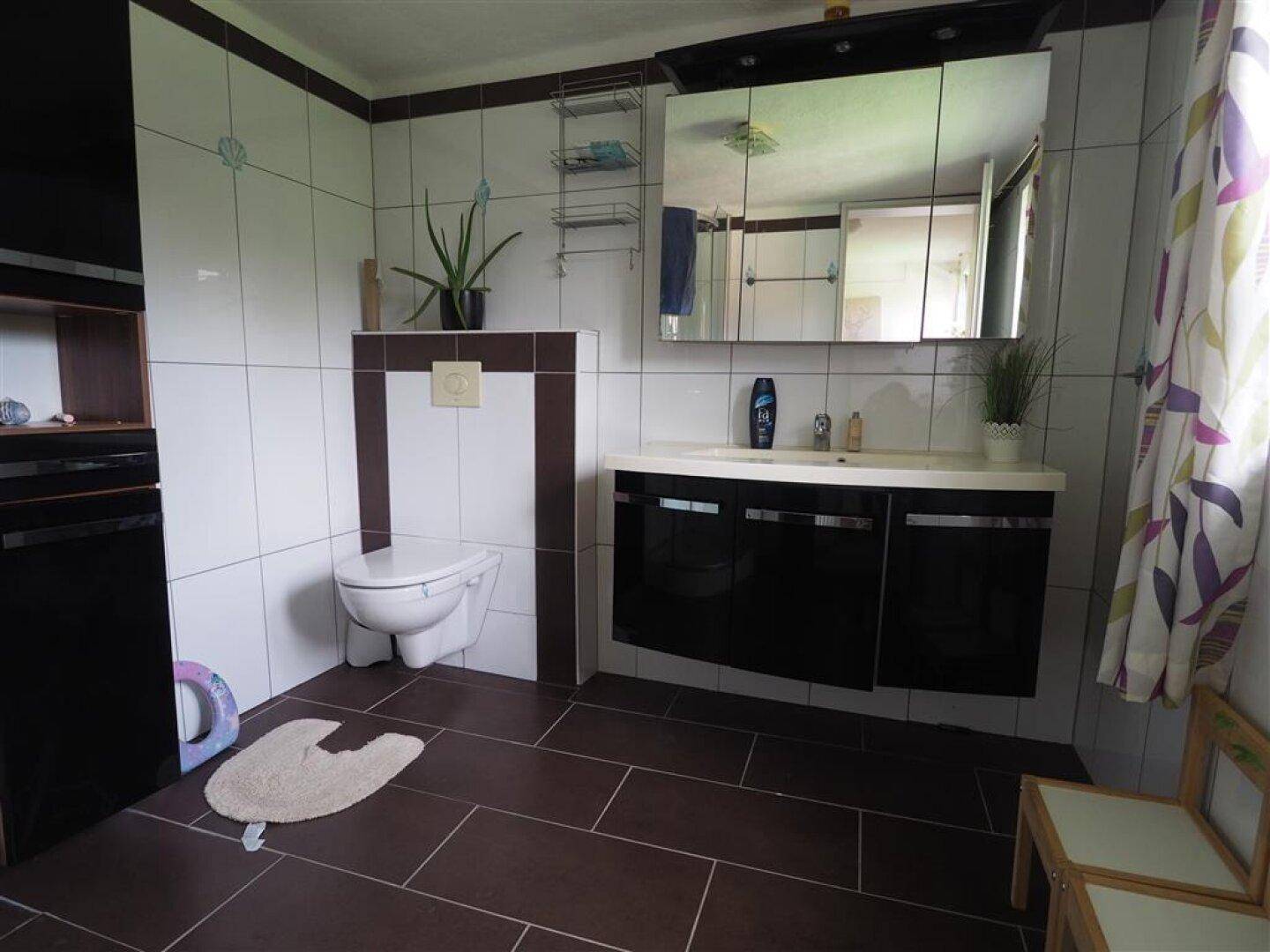 Helles Badezimmer mit Duschkabine, Wand-WC und großem Spiegelschrank.