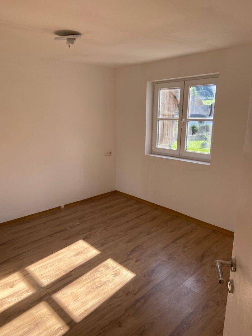 Leeres Zimmer mit hellem Holzboden und Fenster, das viel Tageslicht hereinlässt.