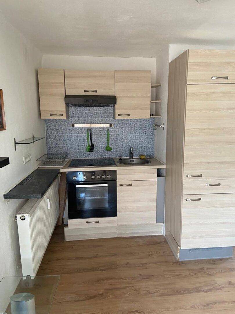 Kompakte Küchenzeile mit hellem Holzboden, Kochfeld und integriertem Kühlschrank.