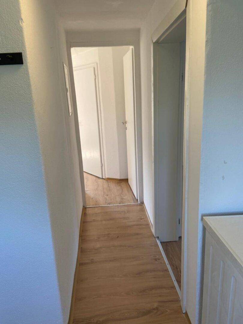 Schmaler Flur mit hellem Holzboden, der zu weiteren Räumen führt.