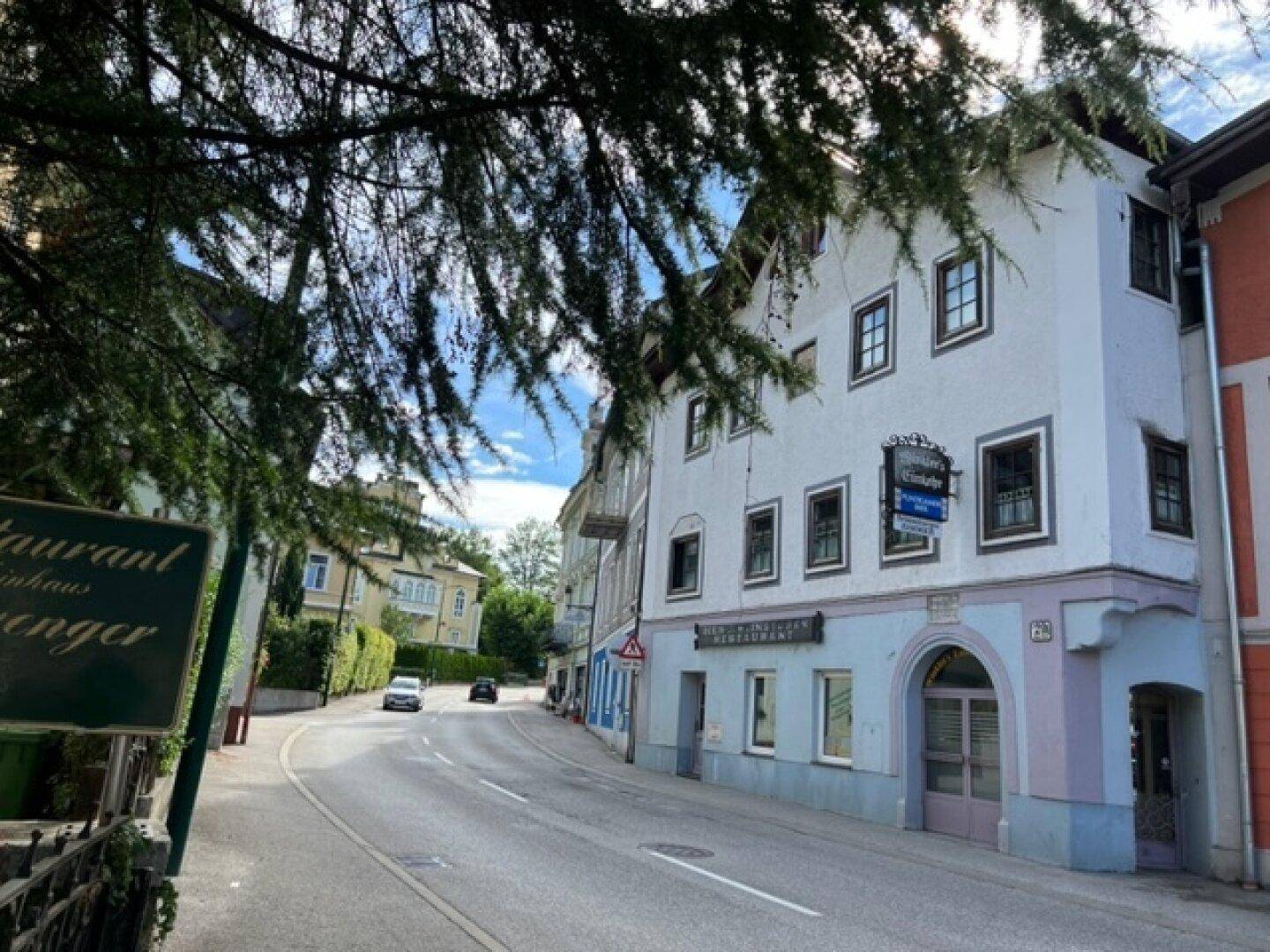 Ansicht des historischen Gebäudes von der Straße mit Bäumen und einem Restaurant-Schild.