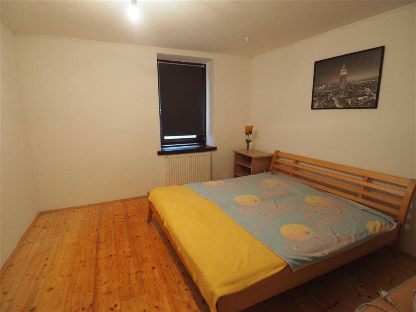 Schlafzimmer mit Holzbett, Holzboden und einem Fenster mit Rollladen.
