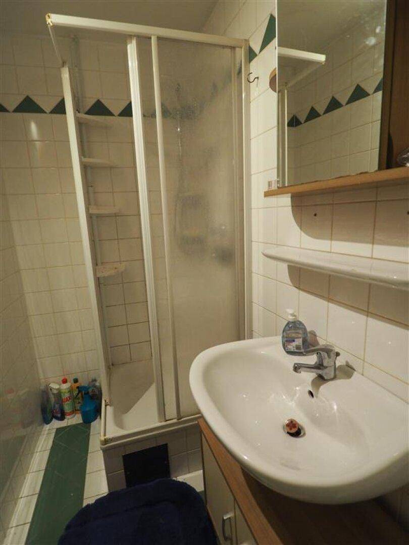 Kleines Badezimmer mit Duschkabine, Waschbecken und weißen Fliesen.