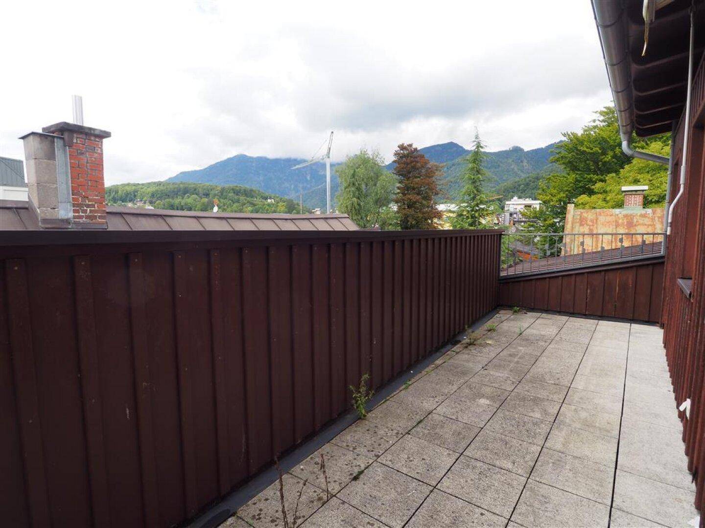 Geräumige Terrasse mit Fliesenboden und Bergblick, umgeben von einer Holzbrüstung.