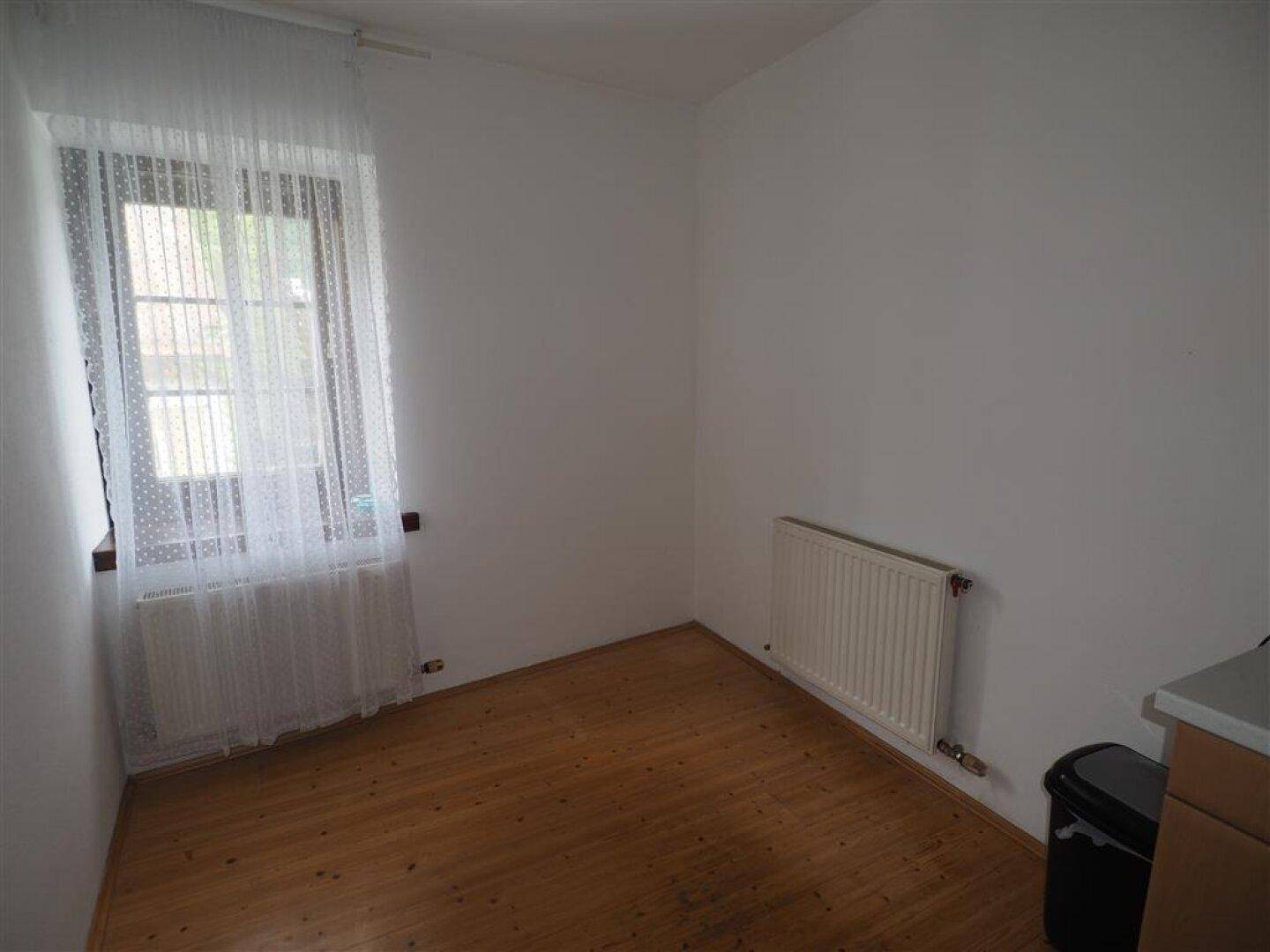 Helles Zimmer mit Holzboden und einem Fenster, das viel Tageslicht hereinlässt.