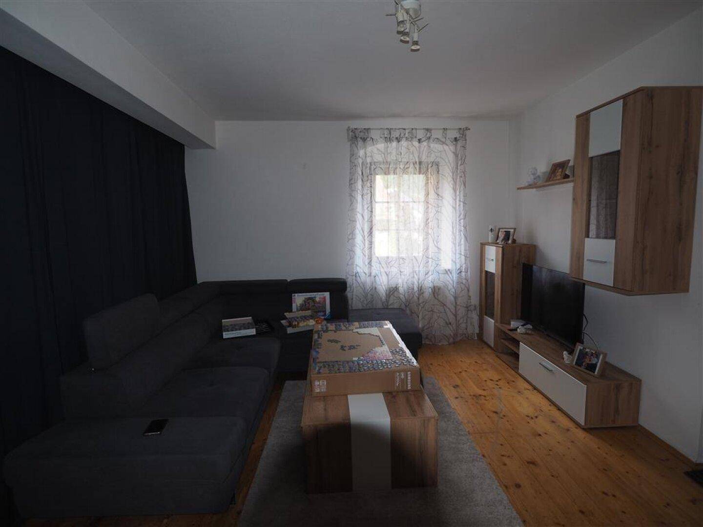 Gemütliches Wohnzimmer mit Sofa, Holzboden und einem Fenster mit Vorhängen.
