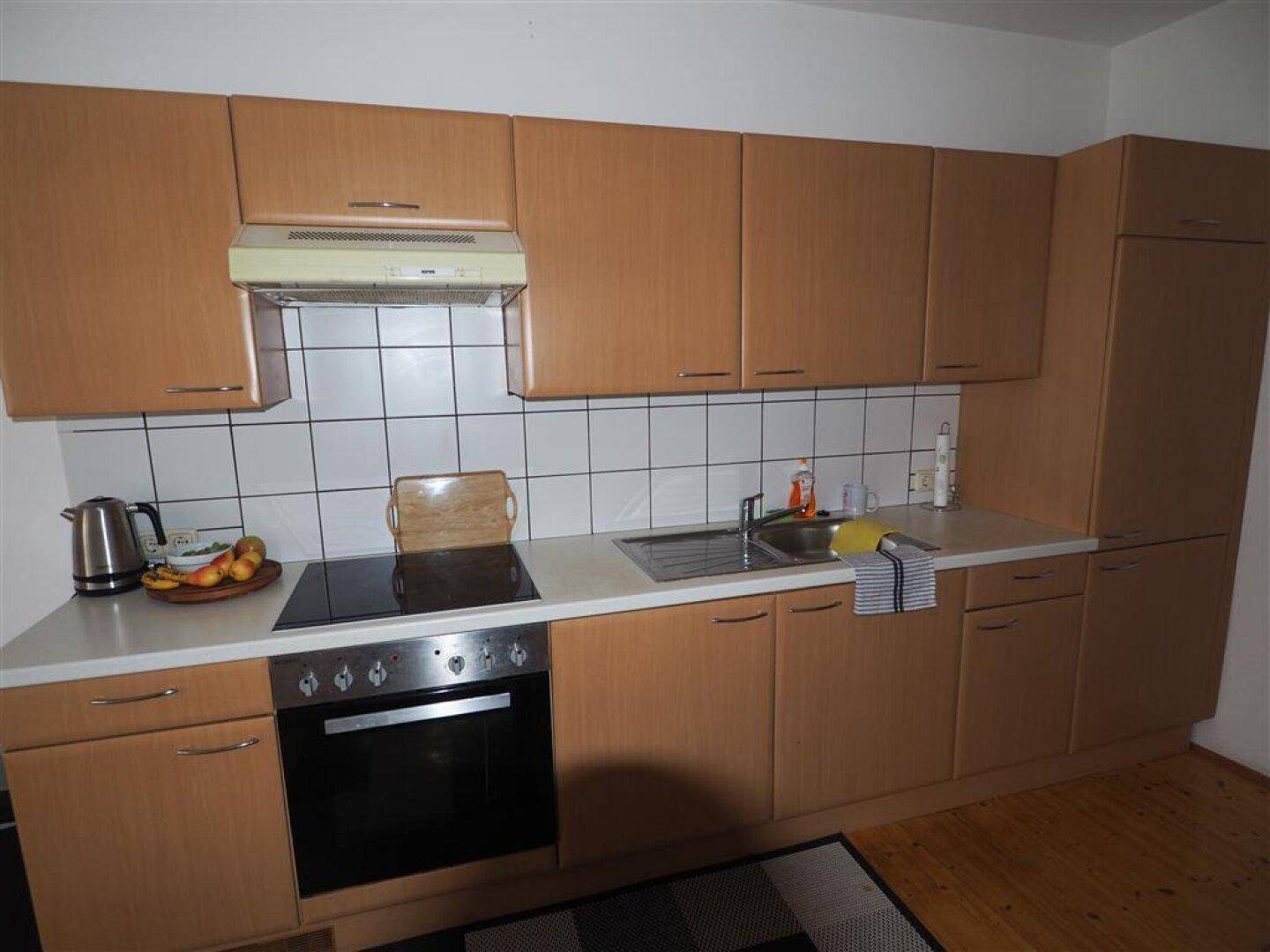 Funktionale Küche mit Holzschränken, Elektroherd und weiß gefliestem Spritzschutz.