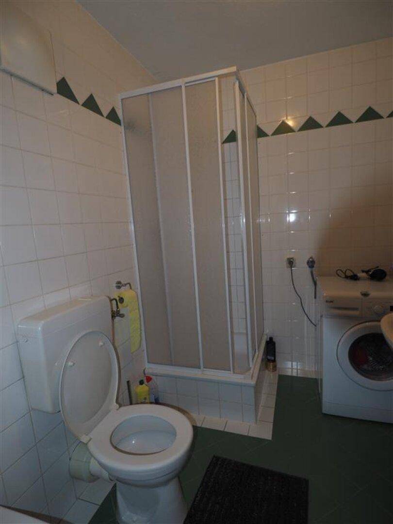 Badezimmer mit Toilette, Duschkabine und Waschmaschine, funktional eingerichtet.