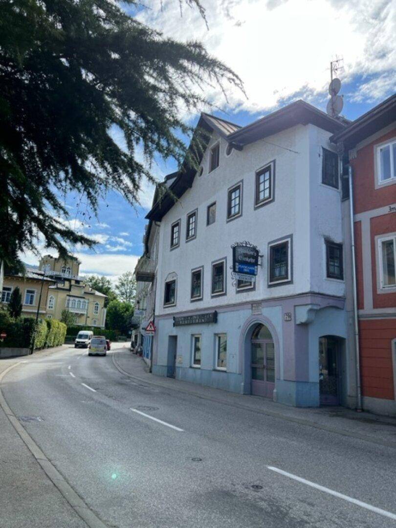 Gebäude an einer Straße mit Geschäften im Erdgeschoss und Wohnungen darüber, umgeben von Bäumen.