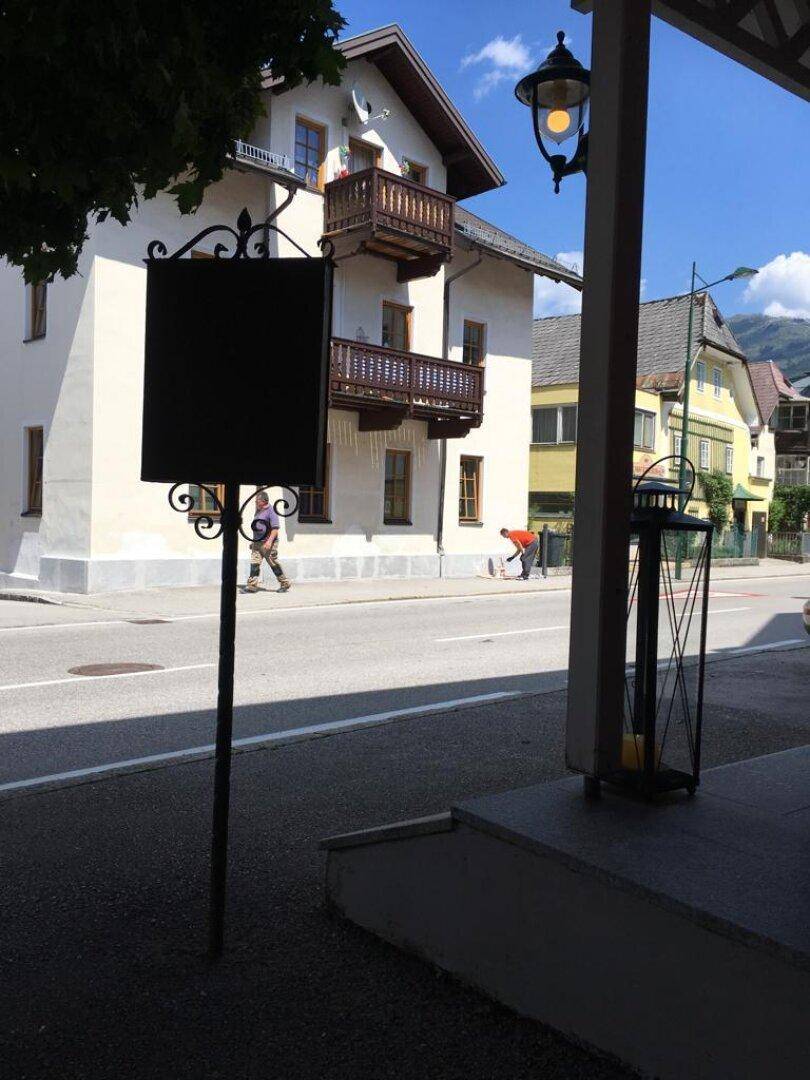 Traditionelles Gebäude mit Holzbalkonen und einem Schild im Vordergrund an einer sonnigen Straße.