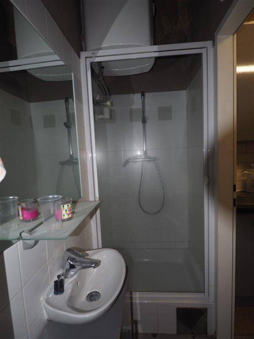 Kompaktes Badezimmer mit Duschkabine und Waschbecken, umgeben von weißen Fliesen und einem Spiegel.