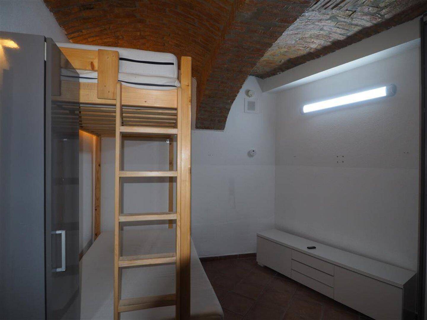 Geräumiges Schlafzimmer mit Etagenbett, Stauraum und Terrakottaboden, beleuchtet von einer modernen Deckenleuchte.