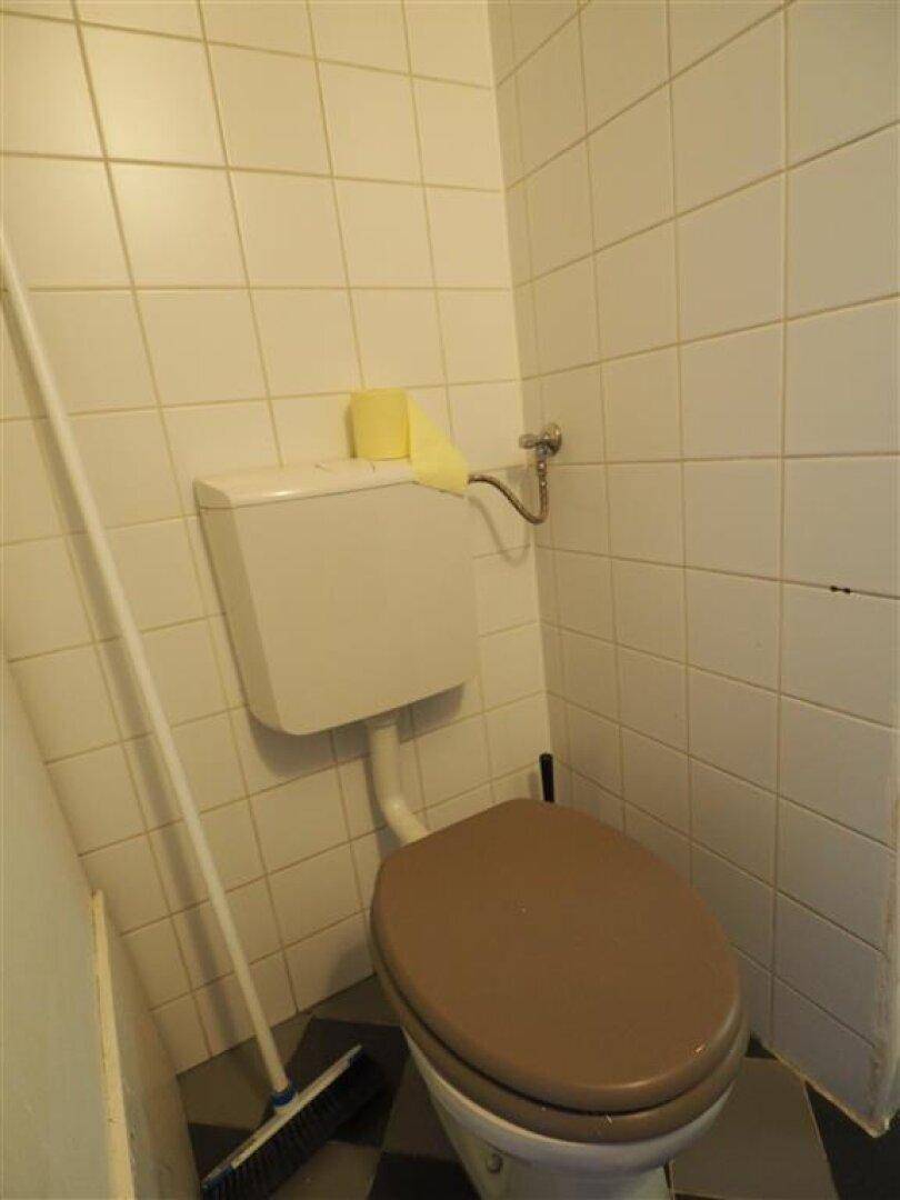 Separates WC mit Toilette und weißen Wandfliesen, ausgestattet mit einem einfachen Besen.