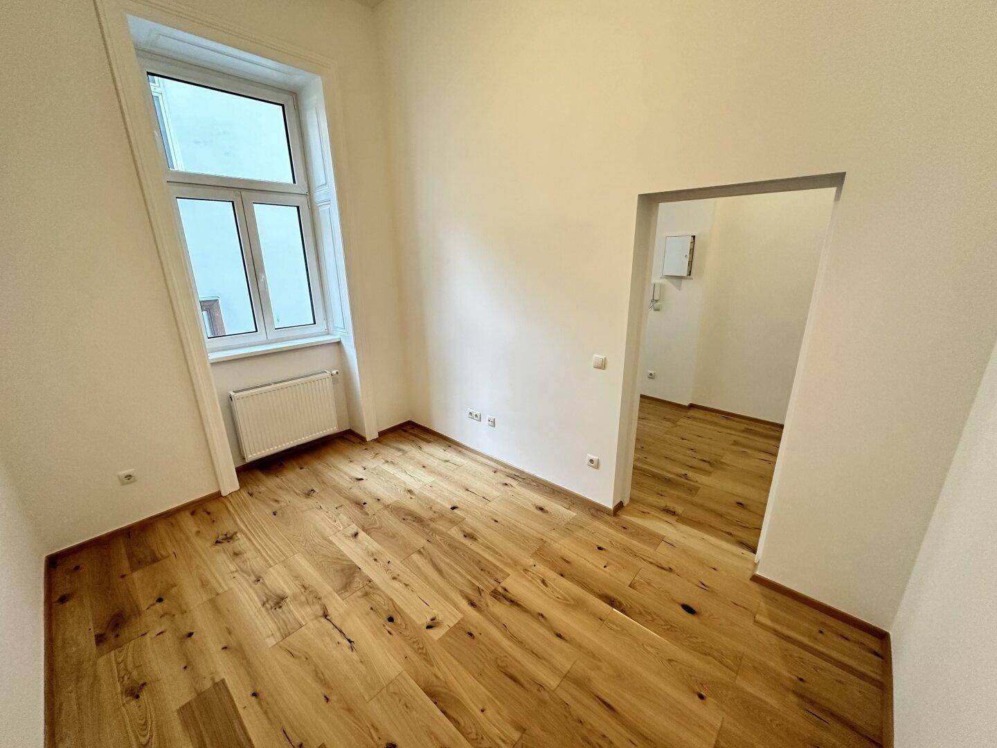 Heller Raum mit Eichenparkettboden und einem Durchgang zu einem weiteren Bereich.