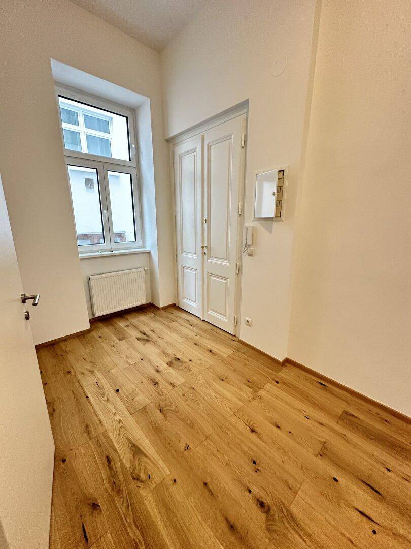 Leerer Raum mit Eichenparkettboden, einem Fenster und einer Doppeltür.