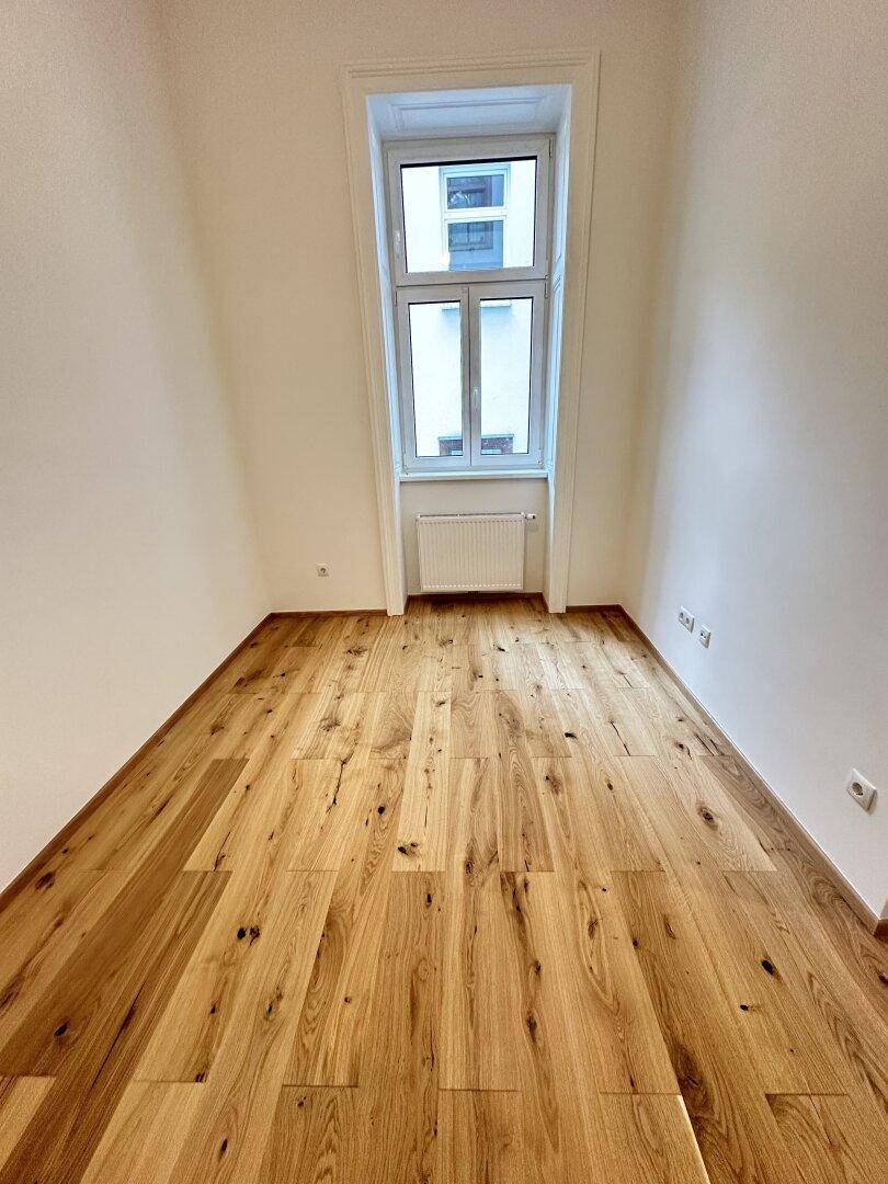 Schmaler, heller Raum mit Eichenparkettboden und einem hohen Fenster.