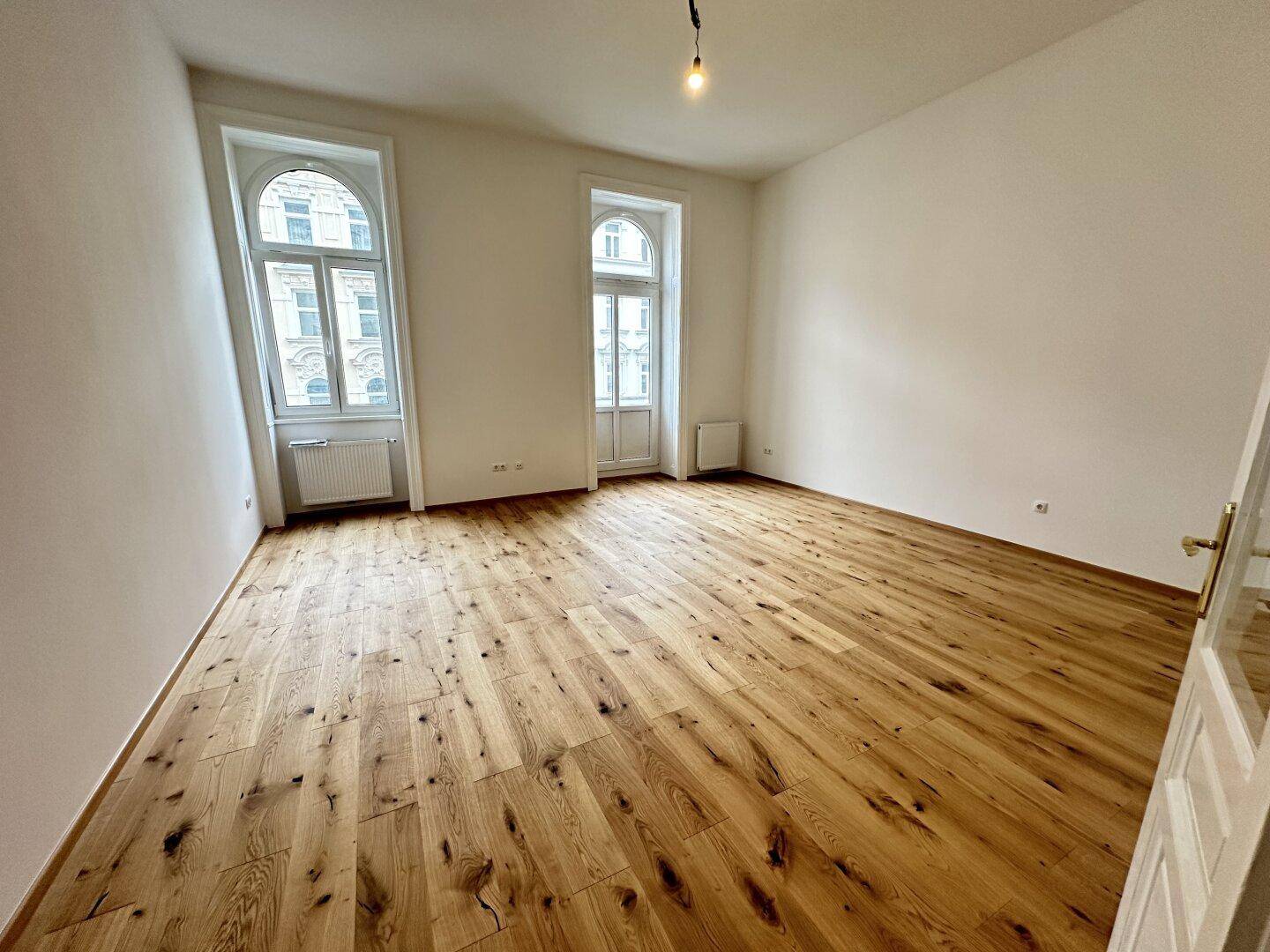 Geräumiges Wohnzimmer mit Eichenparkettboden und zwei hohen Fenstern.