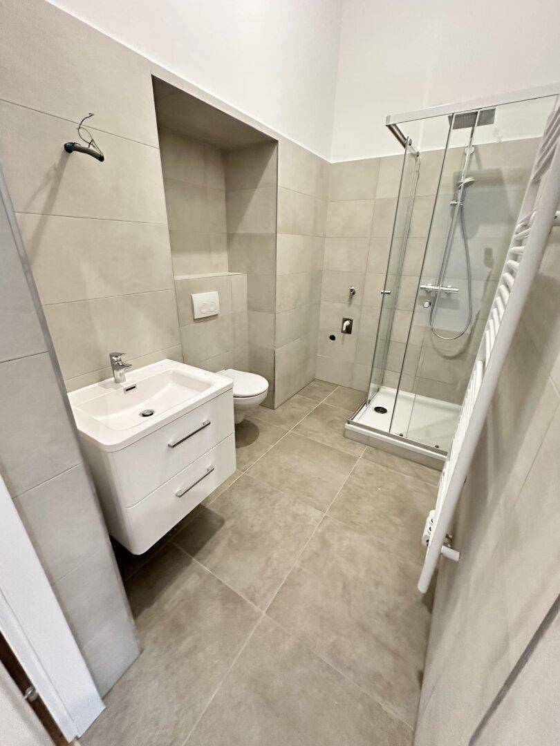 Modernes Badezimmer mit beigefarbenen Fliesen, wandhängendem WC, Waschbecken und Duschkabine.