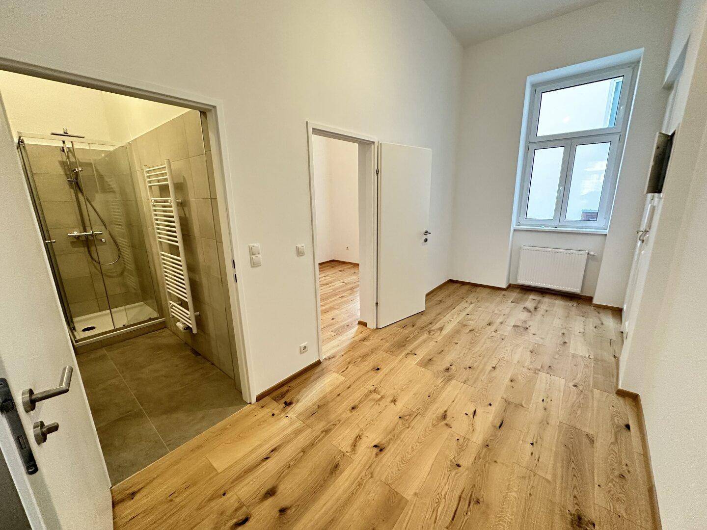 Heller Raum mit Eichenparkett und Zugang zu einem modernen Badezimmer mit Dusche.