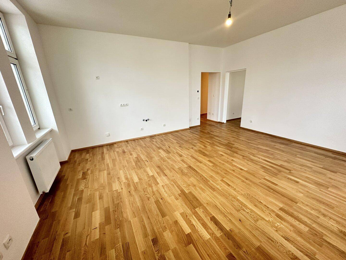 Heller Raum mit Holzboden und Zugang zu weiteren Zimmern, ideal für offenes Wohnen.