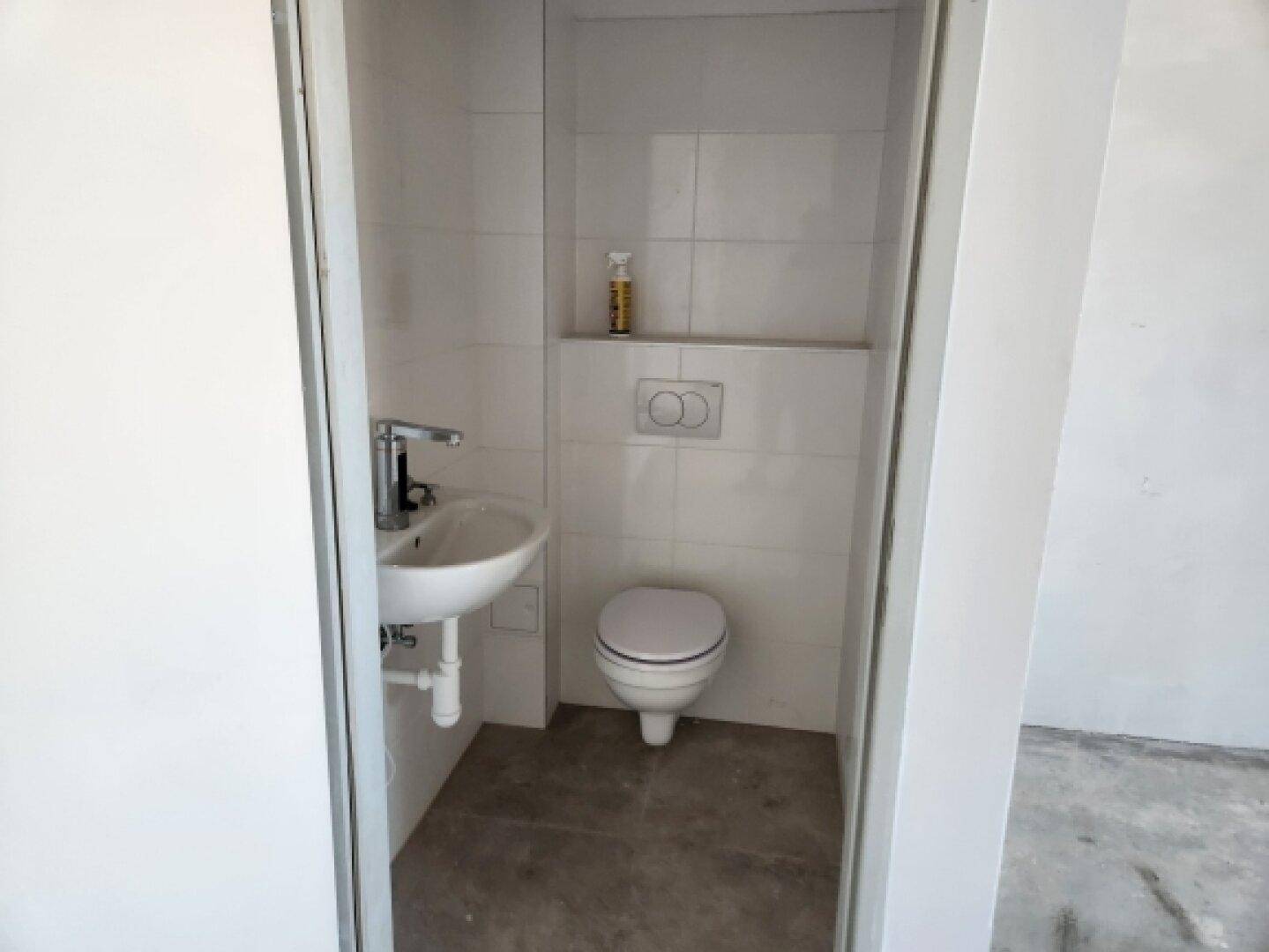 Kleines, modernes Gäste-WC mit wandhängender Toilette und Waschbecken in einem weiß gefliesten Raum.
