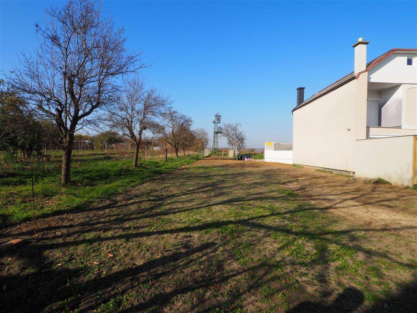 Seitenansicht eines Hauses mit angrenzendem Grundstück und Bäumen unter klarem Himmel.