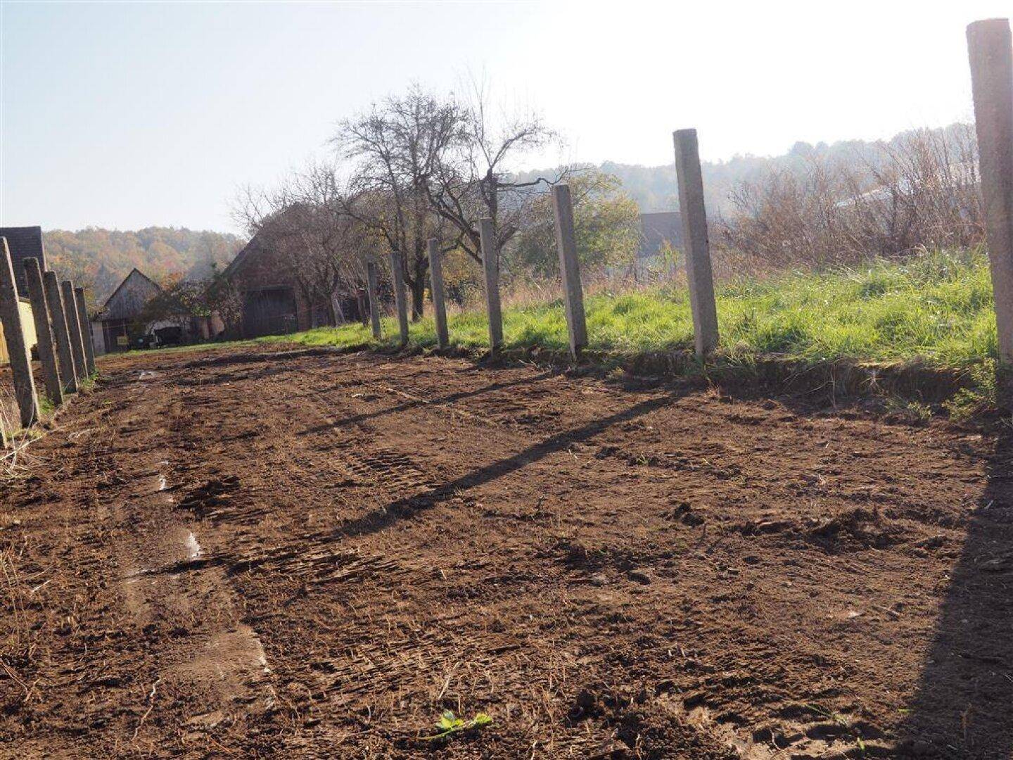 Unbefestigter Weg mit Betonpfosten und ländlicher Umgebung unter hellem Herbsthimmel.