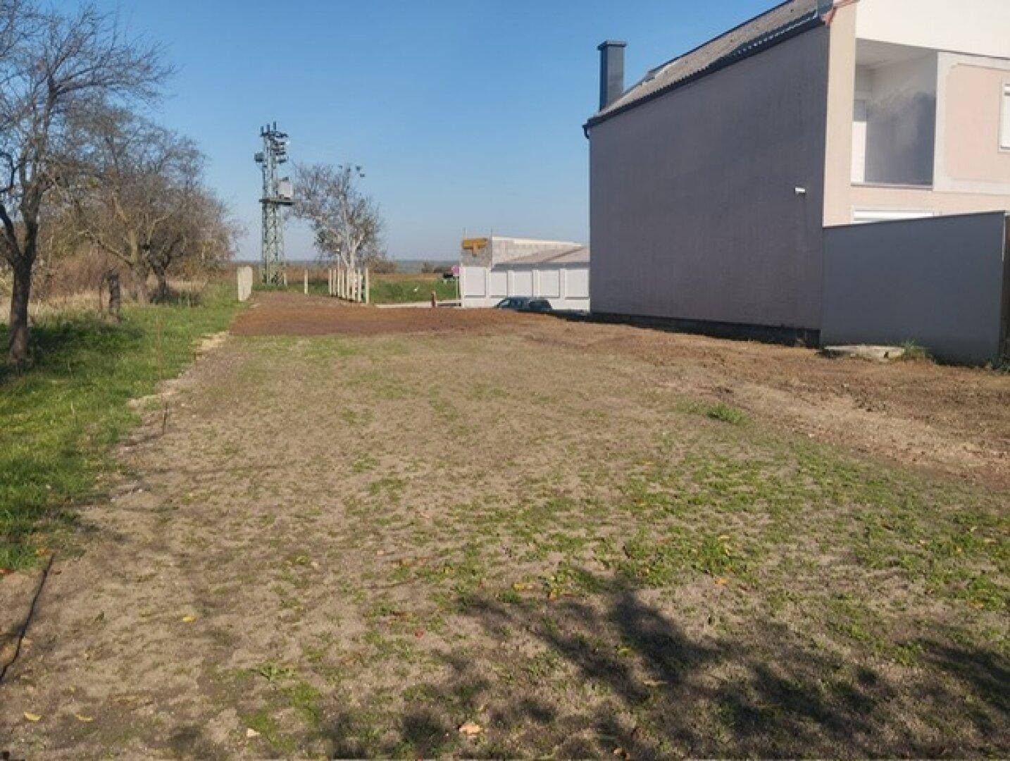 Grundstück neben einem modernen Haus mit teilweise bewachsenem Boden und sonnigem Wetter.