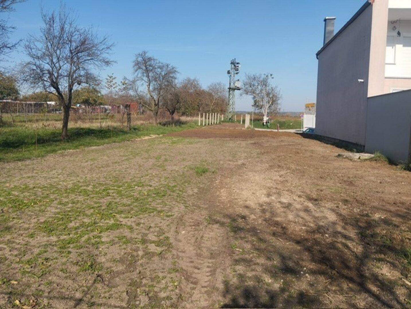 Sonniges Grundstück neben einem modernen Gebäude mit teilweise bewachsenem Boden und klarem Himmel.