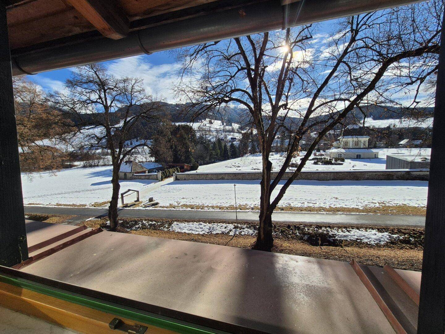 Winterliche Aussicht auf verschneite Felder und Berge unter strahlend blauem Himmel.