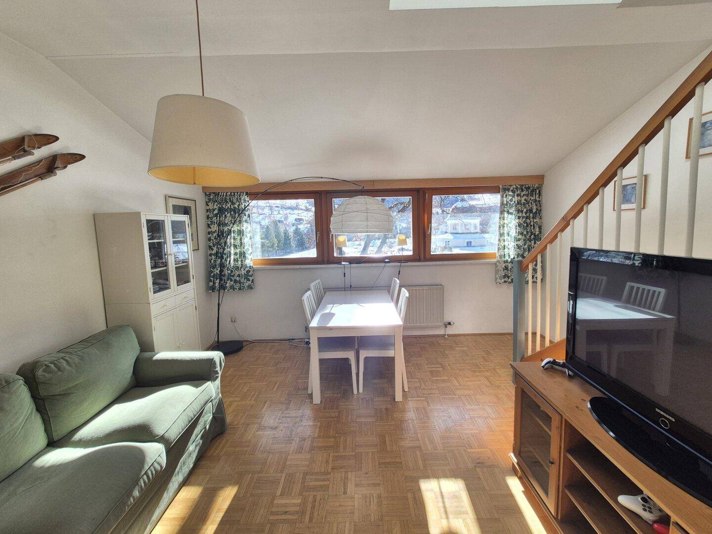 Sonniger Wohn- und Essbereich mit Parkettboden, Sofa und weitem Blick ins Grüne.