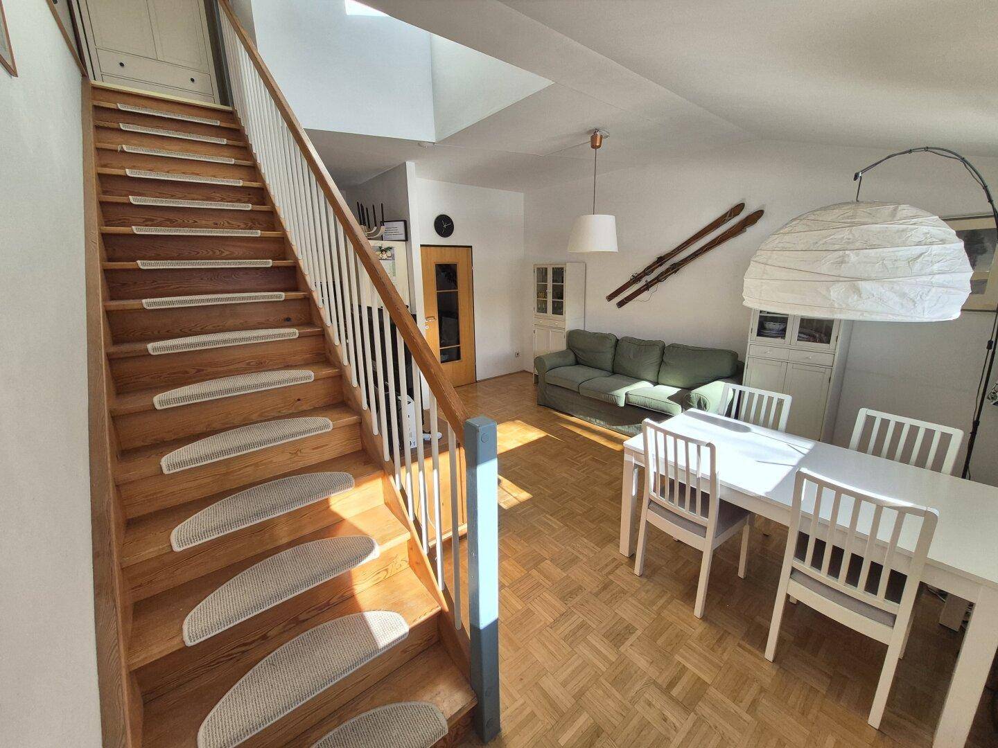 Helle Holztreppe mit Blick auf den Essbereich und das Sofa, lichtdurchflutet.